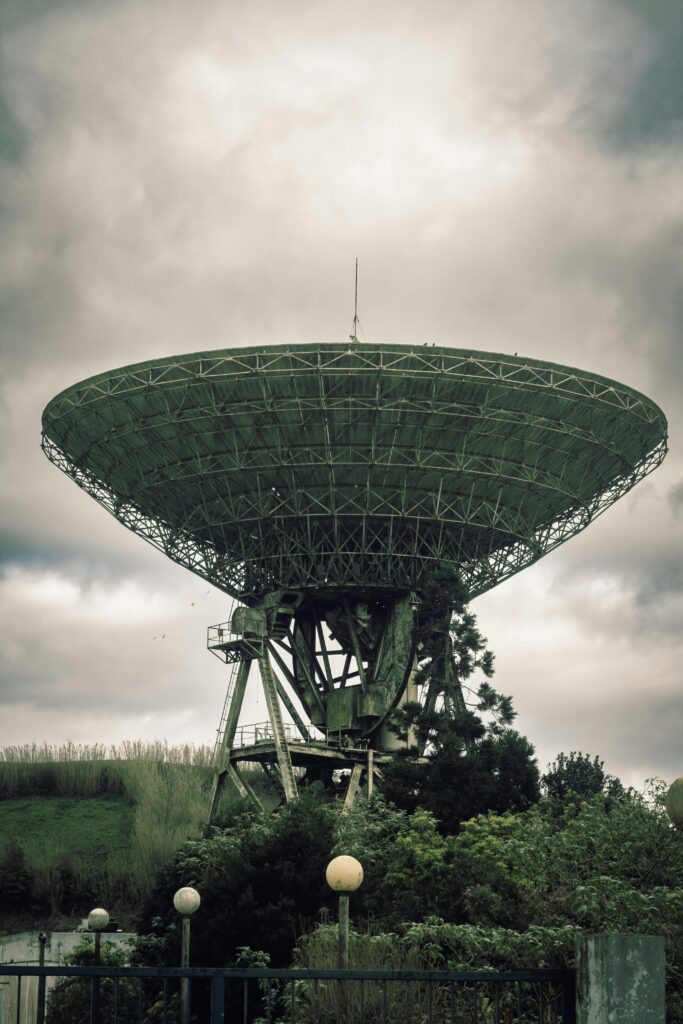 A vintage satellite dish antenna in a lush rural environment under cloudy skies.